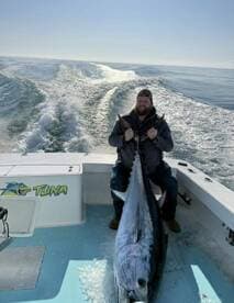 Angler proudly displaying a large Bluefin Tuna on a boat, showcasing a successful offshore fishing trip.