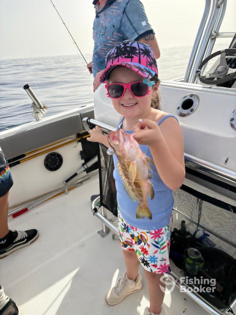 A young girl proudly displaying her catch, a colorful fish, while fishing on a boat, showcasing a fun family fishing experience.