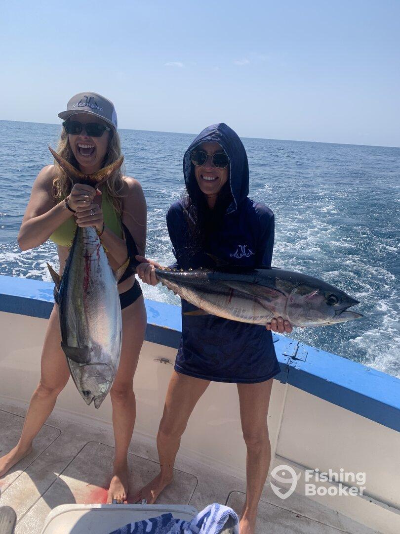 Two anglers proudly displaying their catches of large tuna while enjoying a sunny day on the water.