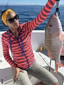 Angler proudly displaying a large Snapper while fishing on a sunny day at sea.