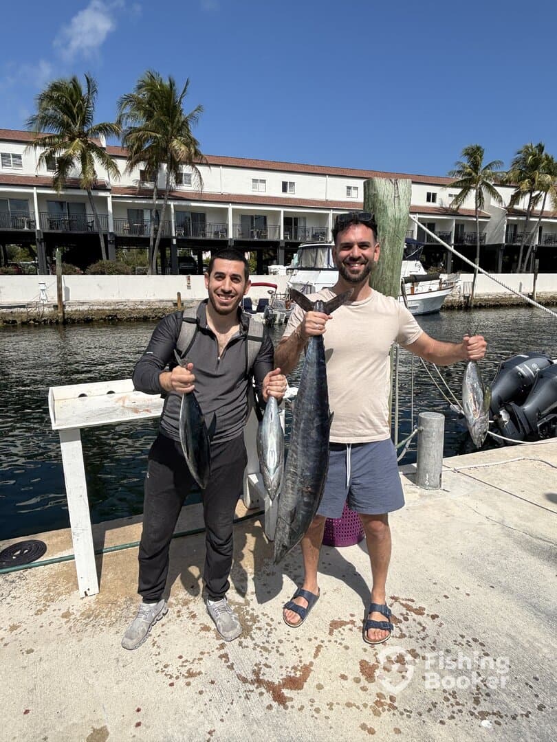 Two anglers proudly displaying their catch of multiple fish, including a large Mahi Mahi, at the dock in a tropical fishing environment.