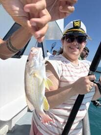 A smiling angler proudly displays a freshly caught fish while fishing on a sunny day, showcasing a fun group fishing experience.