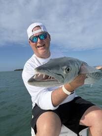 Angler proudly displaying a large Barracuda while fishing in open waters, showcasing a sunny day on the boat.