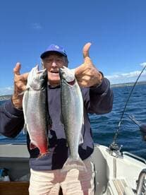 An enthusiastic angler proudly displaying two freshly caught Rainbow Trout while fishing on a boat.