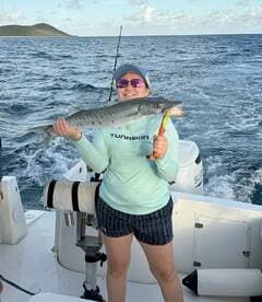 A young angler proudly displaying a large Barracuda while fishing on a boat in open waters.