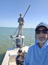 A group of anglers on a boat, with one person standing on the console and another seated, enjoying a day on the water.