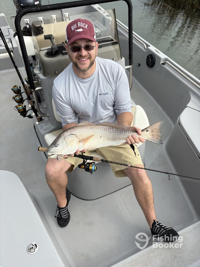 Angler proudly displaying a large Redfish while seated on a fishing boat, showcasing a successful day on the water.