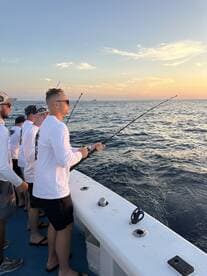 Group of anglers actively fishing at sunset on a charter boat, showcasing a vibrant ocean backdrop.