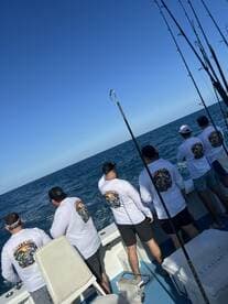 Group of anglers fishing from a boat, casting lines into the open ocean under clear blue skies.