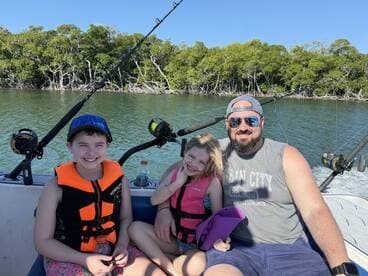 A family enjoying a day on the water, with two children wearing life jackets and a parent on a boat surrounded by mangroves.
