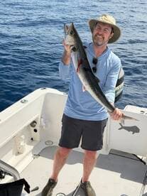 Angler proudly displaying a large King Mackerel on a fishing boat in open waters.