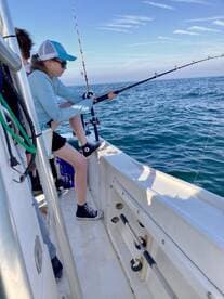 A young angler focused on reeling in a catch while fishing on a boat in open waters.