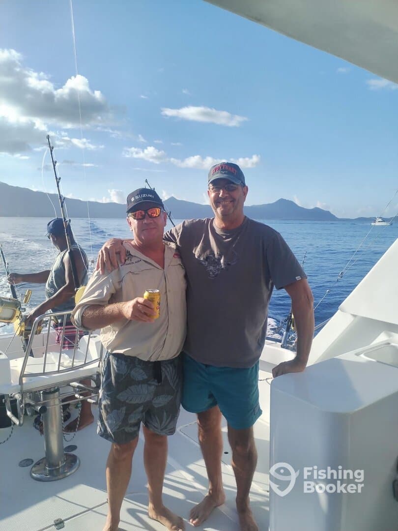 Two anglers enjoying a moment aboard a fishing boat, with a scenic backdrop of mountains and ocean.