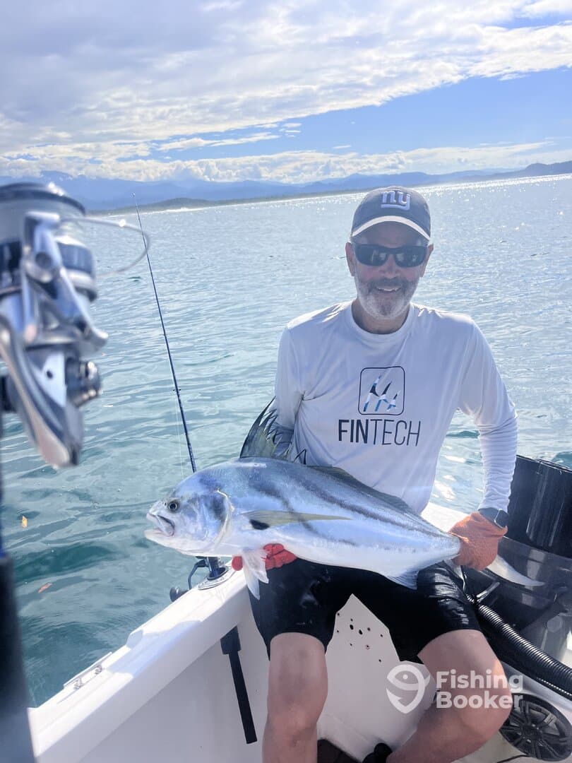 Angler proudly displaying a large fish while fishing from a boat in a scenic coastal environment.