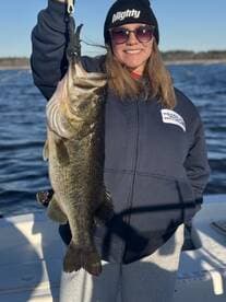 Angler proudly displaying a large Largemouth Bass while fishing on a serene lake.