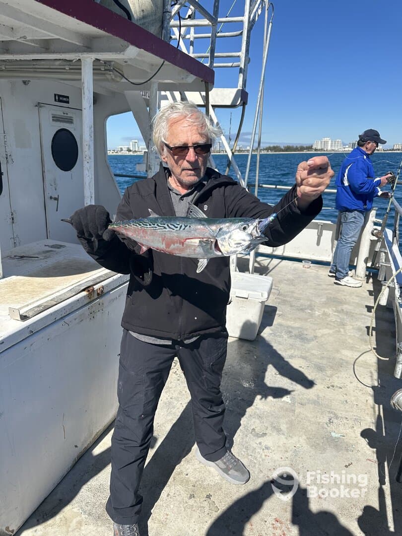 An angler proudly displaying a Mackerel while fishing on a charter boat, with a scenic coastal backdrop.