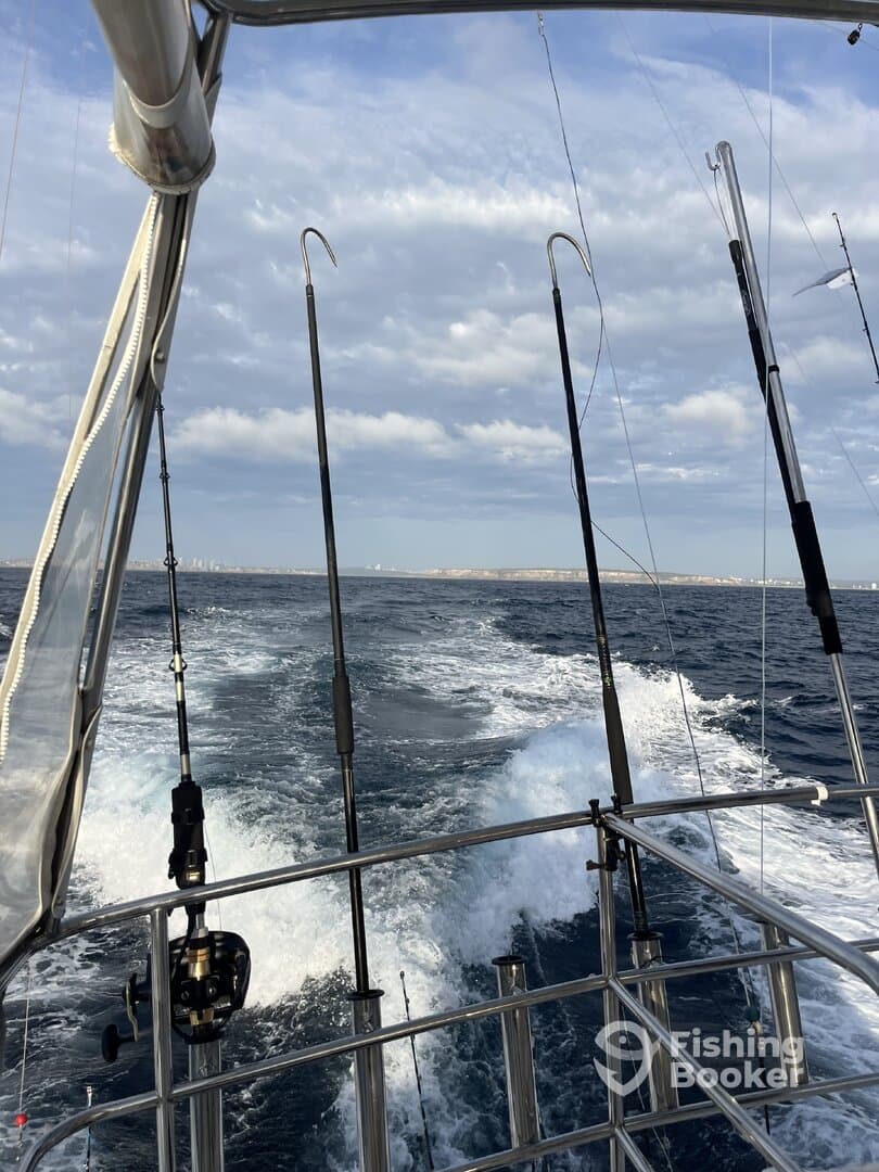 View from the side of a fishing boat with multiple rods set up, cruising through open waters under a cloudy sky.