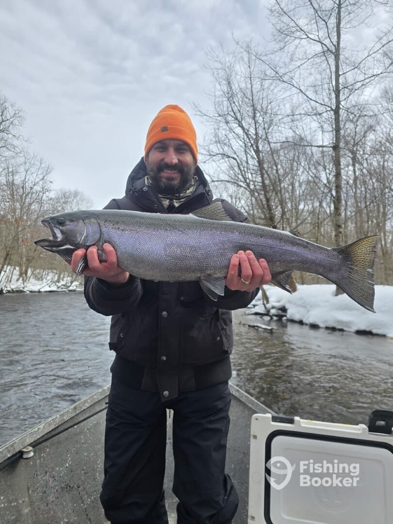 Angler proudly displaying a large Steelhead trout while fishing in a snowy river environment.