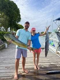 Happy anglers showcasing their impressive catch of a Mahi Mahi and a Wahoo at the dock after a successful fishing trip.