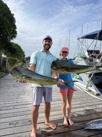 Two anglers proudly displaying their catch of Mahi Mahi on the dock after a successful fishing trip.