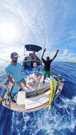 Excited anglers aboard a boat celebrating a catch of Mahi Mahi while fishing in open waters.