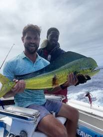 Two anglers proudly displaying a vibrant Mahi Mahi while aboard a fishing boat, showcasing a successful day on the water.