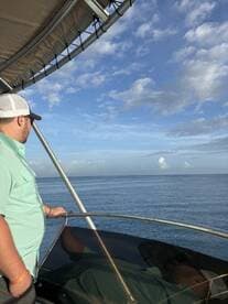 A man enjoying the serene view from the helm of a boat, surrounded by clear skies and calm waters.