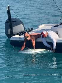 Two anglers working together to release a large tarpon back into the water while fishing from a boat in clear blue waters.