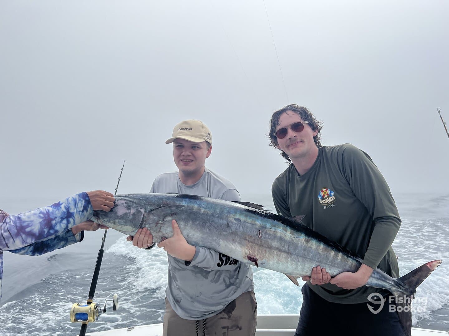 Two anglers proudly displaying a large Wahoo while fishing offshore in foggy conditions.