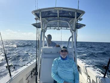 Two anglers enjoying a day on a center console boat, with one seated at the helm and the other navigating the waters.