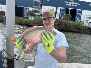 Young angler proudly holding a colorful Snapper at the dock, showcasing a successful fishing trip.