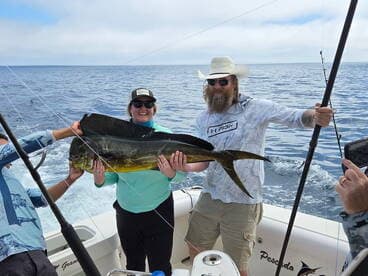 Two anglers proudly displaying a large Mahi Mahi aboard a fishing boat, showcasing a successful day on the water.