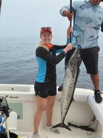 A proud angler holding a large Wahoo on a fishing boat, showcasing a successful catch during a foggy day at sea.