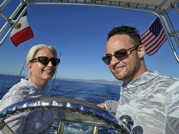 A couple enjoying a sunny day on a fishing boat, with the Mexican and American flags visible in the background.
