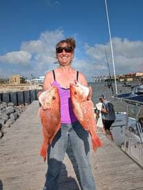 A proud angler displaying two large Red Snapper on the dock after a successful fishing trip.