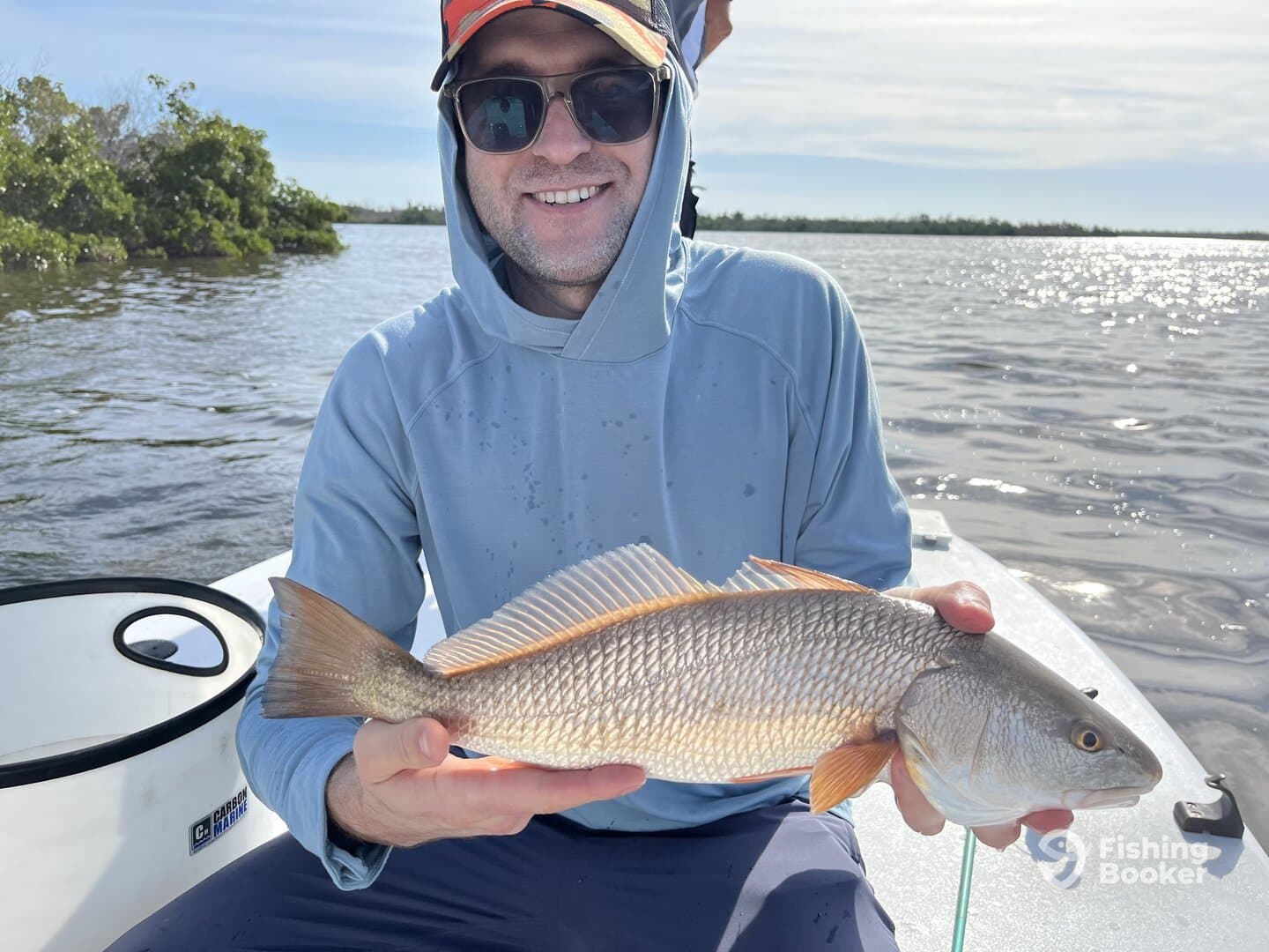Angler proudly displaying a Redfish while fishing in a scenic coastal environment.