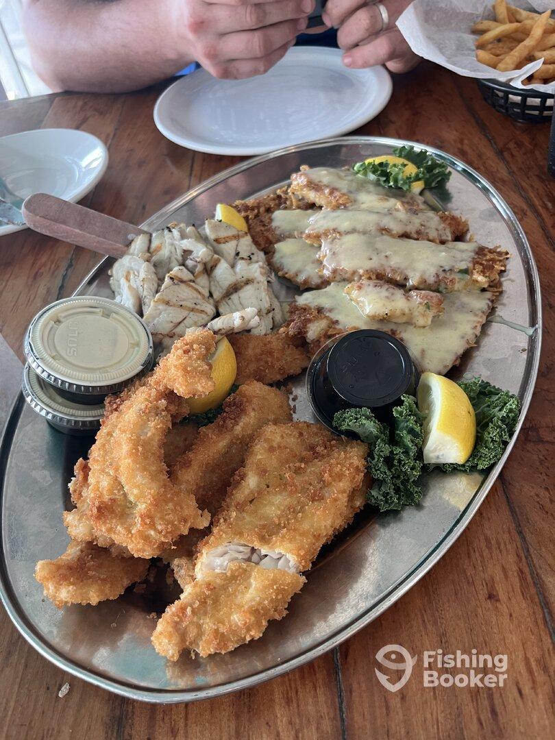 A platter of fried fish and grilled fish fillets served with lemon and dipping sauces, likely enjoyed at a seafood restaurant.
