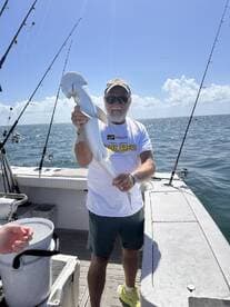 An angler proudly displaying a caught shark while fishing on a boat in sunny waters.