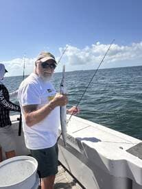 An angler proudly displaying a Barracuda while fishing on a charter boat in sunny waters.