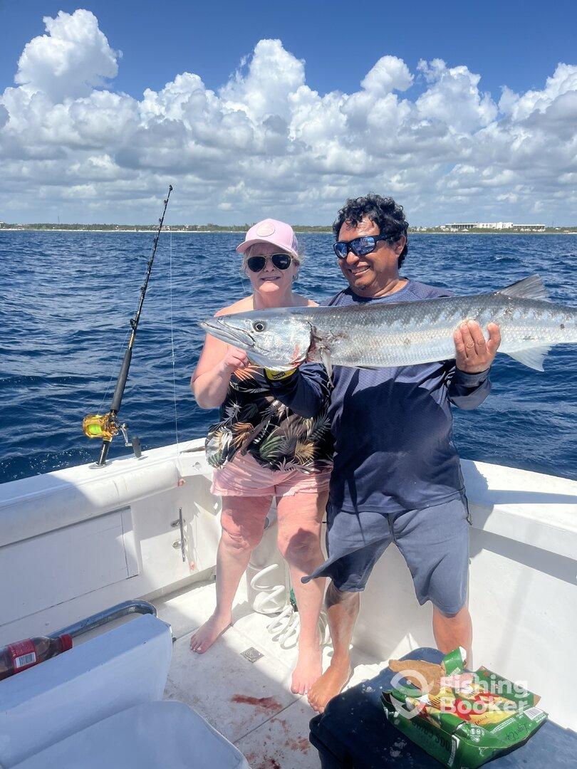 Two anglers proudly displaying a large Barracuda while fishing on a boat, enjoying a sunny day on the water.