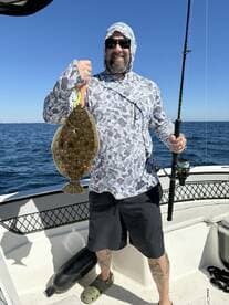 Angler proudly displaying a large Flounder while fishing on a sunny day.