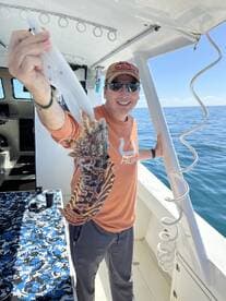 Angler proudly displaying a large lobster while fishing on a boat in clear waters.