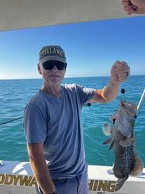 An angler proudly displaying a large Grouper while fishing on a boat in clear blue waters.
