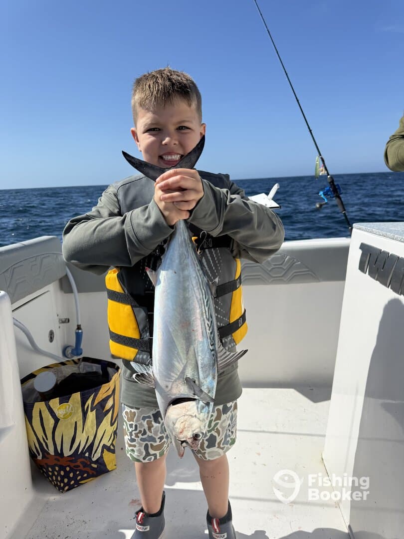 A young angler proudly displaying a caught fish while aboard a fishing boat, showcasing a sunny day on the water.