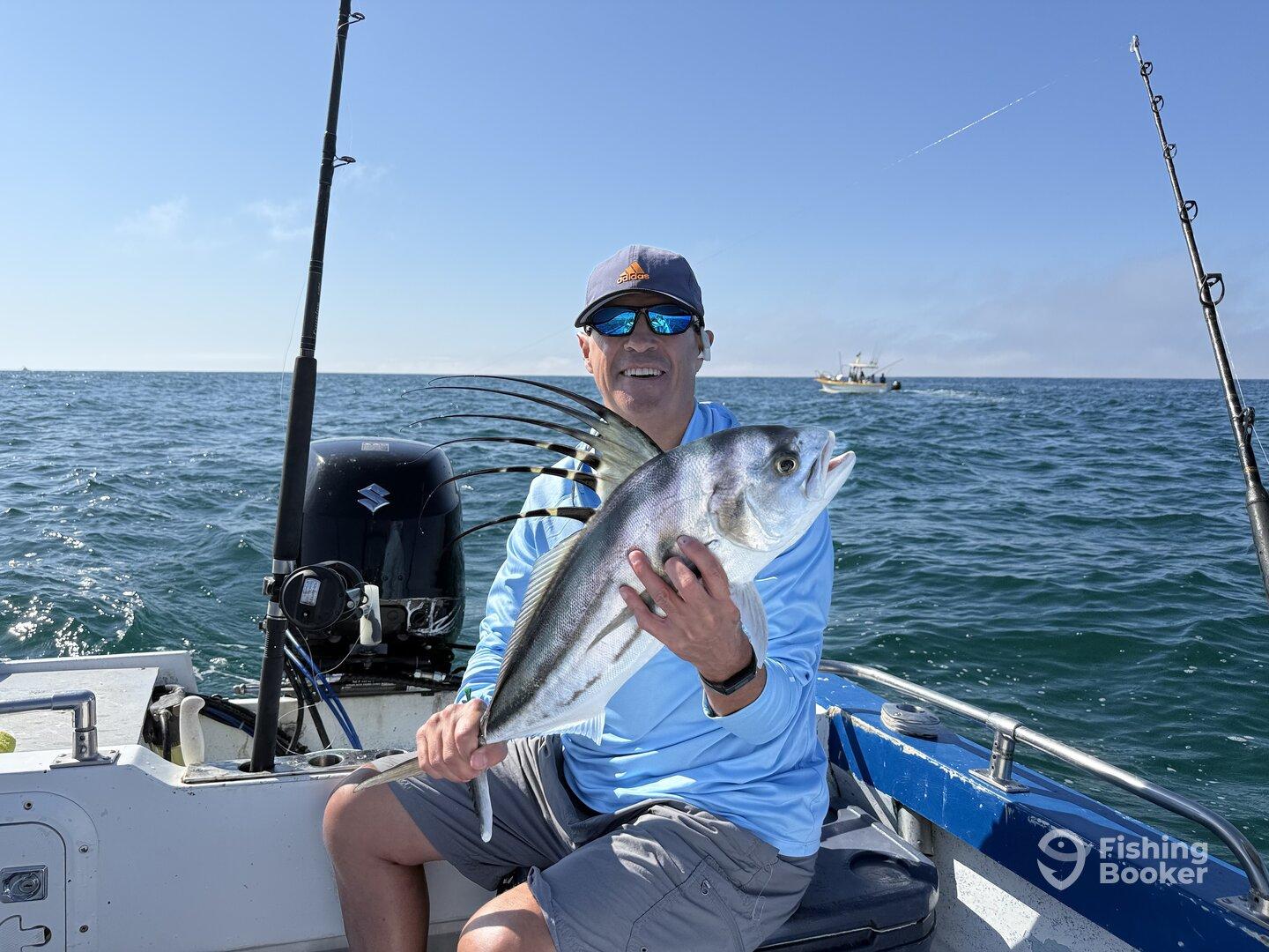 Angler proudly displaying a large Blackfin Tuna while fishing on a boat in clear waters.