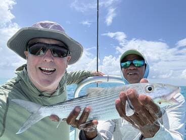 Two anglers proudly displaying a large Bonefish while enjoying a sunny day on the water.