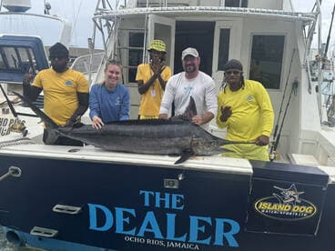 A group of anglers proudly displaying a large Marlin on the boat 'The Dealer' in Ocho Rios, Jamaica, showcasing a successful fishing trip.