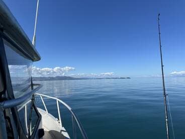A serene view of the boat's exterior on calm waters, showcasing the clear blue sky and distant mountains.
