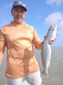 Angler proudly displaying a large Speckled Trout while fishing on a sunny day.