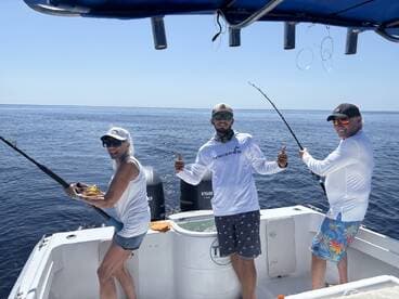 Three anglers actively fishing on a boat, enjoying a sunny day on the water, with one angler reeling in a catch.